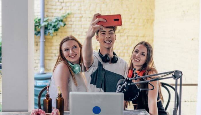 Três criadores de conteúdo gravando reels por selfie juntos, mostrando equipamentos de gravação e um cenário descontraído, representando a criação de conteúdo colaborativo para o Instagram.