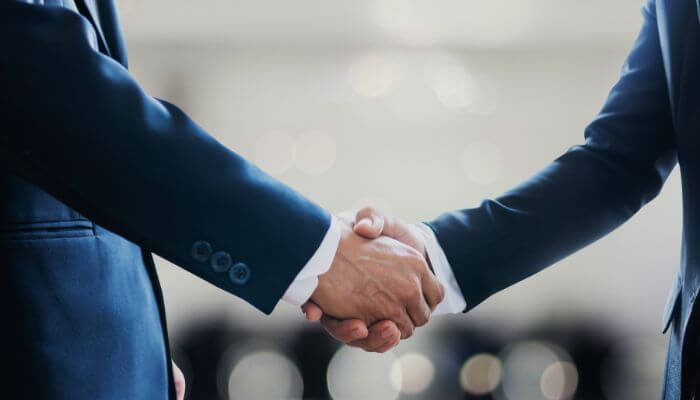 Foto de um aperto de mãos entre duas pessoas vestindo ternos, representando ações para fechar ótimos negócios e parcerias no Instagram.