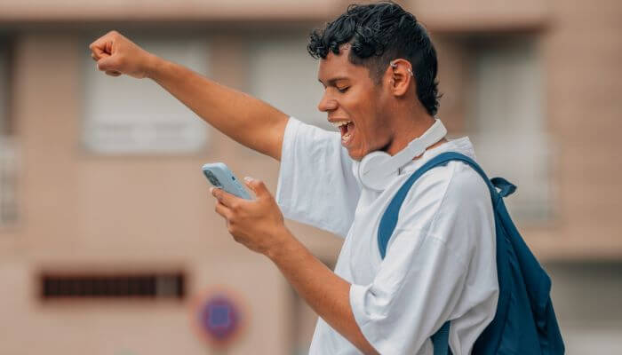 Foto de um homem olhando para seu smartphone e levantando o punho com entusiasmo, representando uma estratégia de divulgação no Instagram.