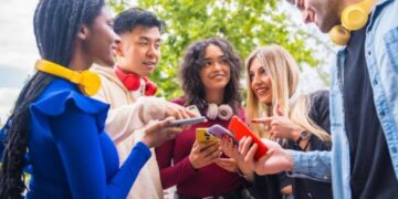 Grupo de jovens segurando smartphones e usando fones de ouvido coloridos, representando como colocar música no Instagram em posts, Stories e Reels.