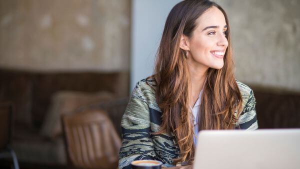 Mulher sorrindo enquanto trabalha em um notebook em um ambiente de café.