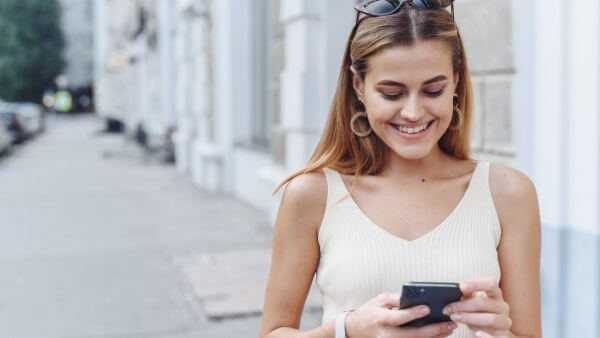 Uma mulher sorrindo verificando seu celular ao ar livre, aproveitando um momento agradável.