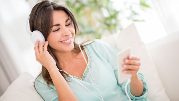 Mulher feliz escutando música com fones de ouvido no sofá.