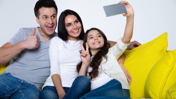 Família sorridente tirando uma selfie juntos no sofá, capturando um momento de felicidade em casa. Bio para instagram infantil feminino