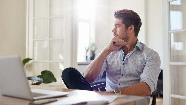 Homem olhando pela janela e pensando enquanto está sentado diante do laptop. Nomes para instagram masculino