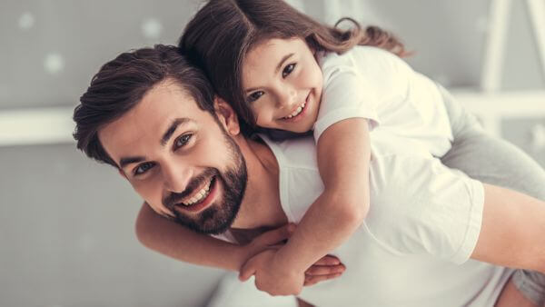 Pai dando uma carona nas costas para sua filha, ambos sorrindo felizes.