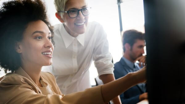 Duas mulheres trabalhando juntas no escritório, uma delas apontando para a tela do computador. Overposting

