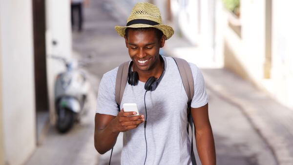 Jovem usando chapéu e fones de ouvido, sorrindo enquanto olha para o celular.