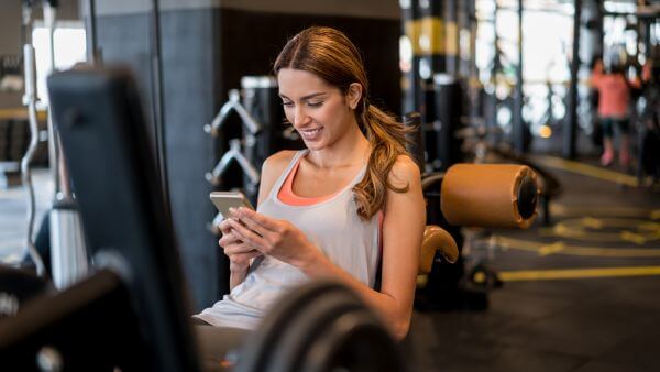 Mulher em uma academia usando o celular, sorrindo enquanto navega no Instagram.