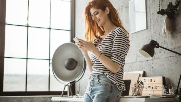 Mulher sorrindo enquanto utiliza o celular, representando satisfação ao configurar a ocultação de curtidas no Instagram.