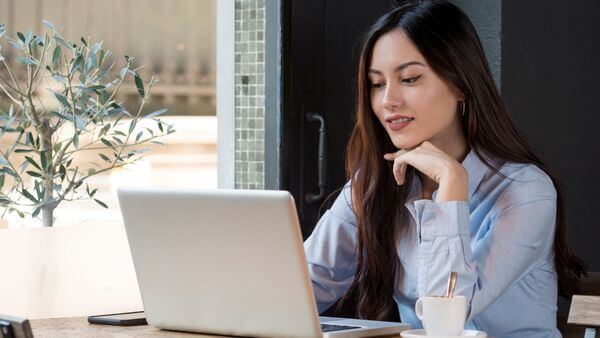 Jovem mulher sorrindo enquanto utiliza um notebook em um café, representando a personalização de conteúdo e paletas de cores para Instagram.