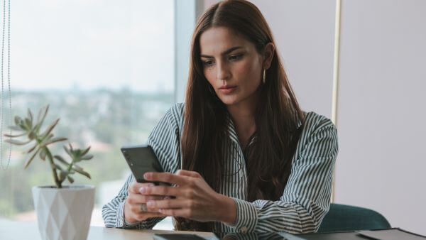 Mulher séria utilizando um smartphone em um escritório moderno, simbolizando a busca por nomes criativos para TikTok.