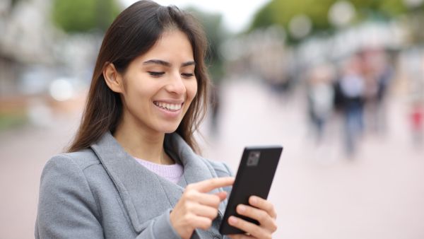 Mulher sorrindo enquanto vê Reels em lugar público após aprender como colocar legenda no Instagram